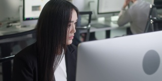 有吸引力的年轻女子在台式电脑上工作，而在大的开放空间办公室工作。正面商业女性的肖像看着室内的电脑屏幕