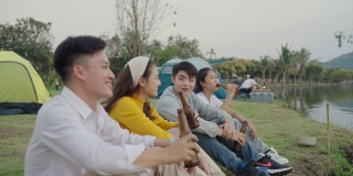 群亚洲四青年朋友男女在河边野餐野营，他们有说有笑，喝着庆祝欢呼啤酒。