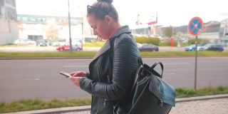 一名女子在城市街道上用手拿着手机。使用移动应用程序
