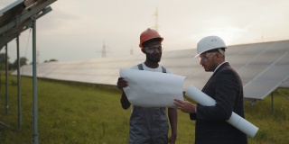 手里拿着图纸的印度技术员向拿着剪贴板的非裔美国检查员展示太阳能工厂。两个人在研究替代能源
