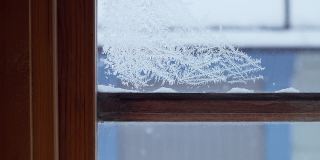 扫过一扇结了冰的窗户，窗户上覆盖着霜和闪亮的冰晶，破旧的木框，外面缓缓降下雪