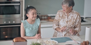 亚裔华人老太太周末在厨房展示和教她的孙女煮饺子