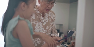 亚裔中国孙女在周末闲暇时间在厨房里跟奶奶学习烹饪技巧