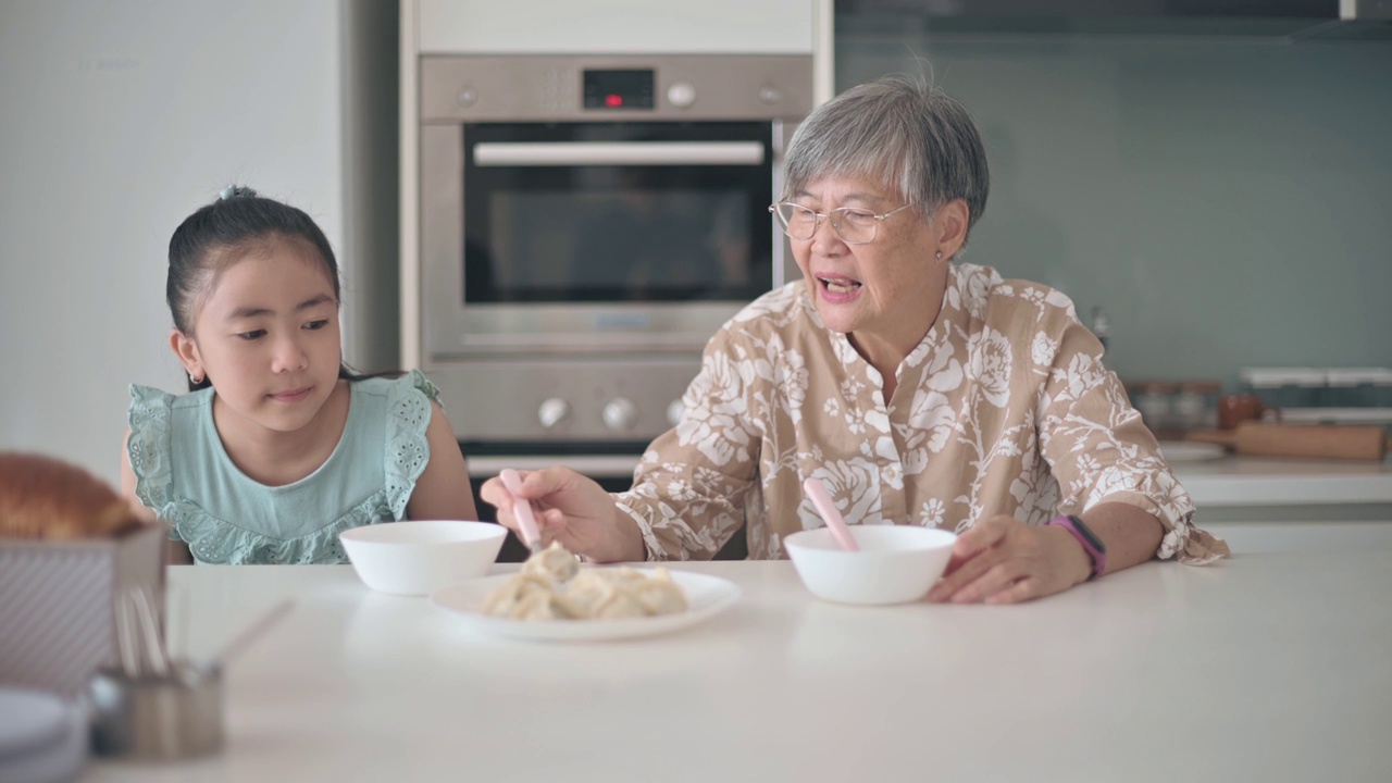 亚裔华人老太太和她的孙女在厨房的柜台上吃饺子