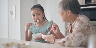 亚裔华人老太太和她的孙女在厨房的柜台上吃饺子