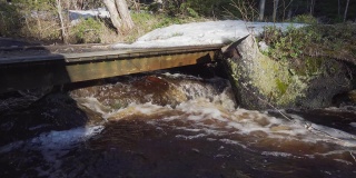 非常小的木桥，在森林小溪上，有很多水流过。流水附近的森林里正在融化积雪。瑞典,欧洲。原来的流水声