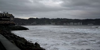 在法国亨达耶，背景是亨达里比，一个灰色的多云的日子，海浪汹涌，海浪拍打着码头的岩石，使海滩消失。白色的泡沫和铅灰色的日子