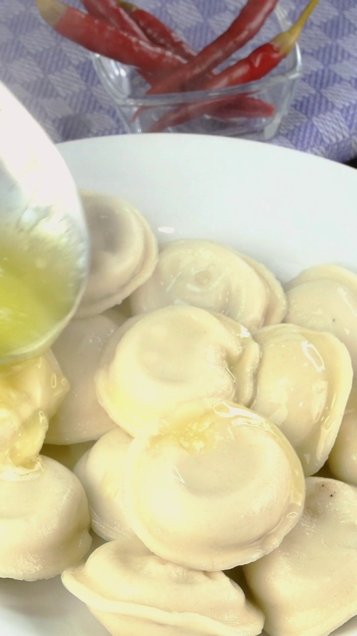 肉饺或馄饨放在白色的碗里，浇上融化的黄油。垂直,特写。