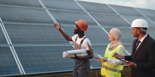 非裔美国技术人员向印度男子和穆斯林妇女展示现代太阳能站。两个经理用笔记本电脑和剪贴板控制绿色能源的生产。太阳能电站技术员