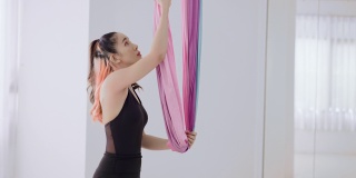 活泼迷人的年轻亚洲女运动员身穿黑色运动服，在彩色吊床上准备表演飞行瑜伽或空中瑜伽或反重力瑜伽，这是结合了传统瑜伽与动作的普拉提，舞蹈和杂技。