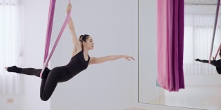 空中反重力瑜伽女人在黑色运动服做瑜伽飞或美人鱼流或伸展美人鱼姿势空中使用彩色丝带。漂亮的空中杂技亚洲妇女表演体育锻炼飞行瑜伽在彩色吊床在健身室。