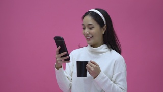 美丽的亚洲女性微笑着用智能手机网购和喝咖啡视频素材模板下载