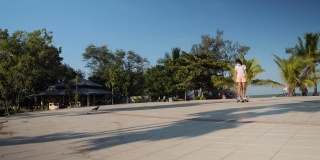 亚洲女孩在公园户外玩冲浪滑板在阳光明媚的日子与椰子树的背景，生活方式的概念。