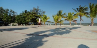 亚洲女孩在公园户外玩冲浪滑板在阳光明媚的日子与椰子树的背景，生活方式的概念。