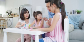 亚洲幼女和父母一起在纸上画画。快乐的家庭活动，小女孩们在客厅里学习画画，和爸爸妈妈一起享受创造力。