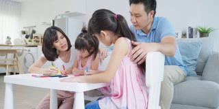 亚洲幼女和父母一起在纸上画画。快乐的家庭活动，小女孩们在客厅里学习画画，和爸爸妈妈一起享受创造力。