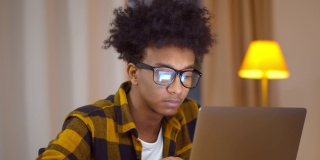 年轻的非洲裔自由职业者，在家里专心地用笔记本电脑工作。年轻的学生戴上眼镜，坐在客厅里的电脑上学习