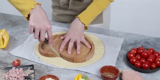 一个穿着黄色毛衣的白人少女的手在一个心形的木盘上用刀切生面团