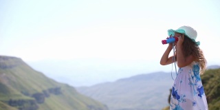 一个小女孩戴着帽子，穿着背心裙，通过望远镜在高山上观看——旅游，环保意识。爬山，积极的生活方式。达吉斯坦,Khunzakh