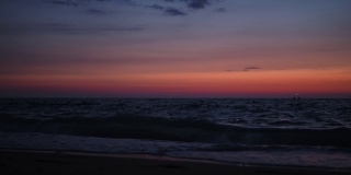 太阳落山后，人们在黄昏时到海里游泳。在远处，可以看到孩子们在波浪上跳跃。好玩的心情。红色的天空