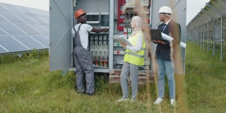 多种族的人在检查太阳能电站的开关。电气系统设备配电柜。多种族的人们审视绿色能源的生产过程。电力变压器