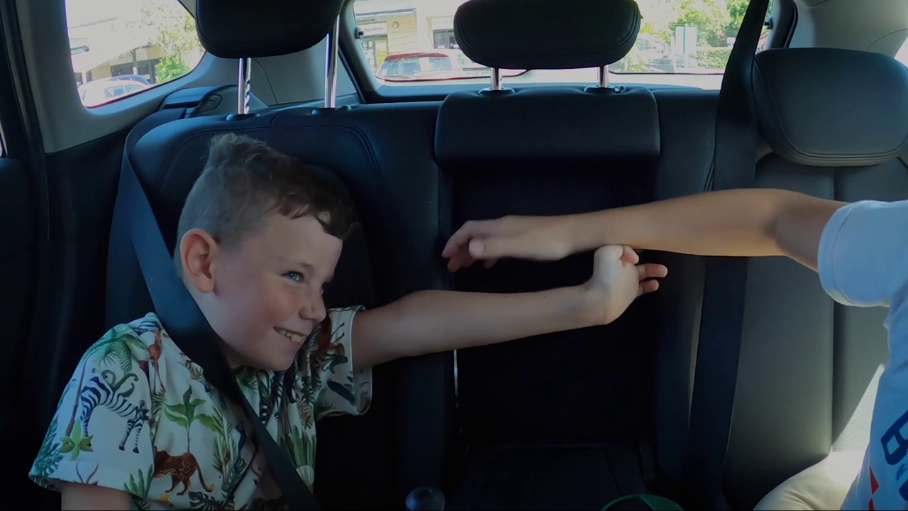 两个男孩在一辆汽车的后座上互相打闹。胳膊和手碰在一起。