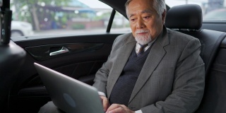 4K亚洲资深商人坐在汽车后座上工作的笔记本电脑