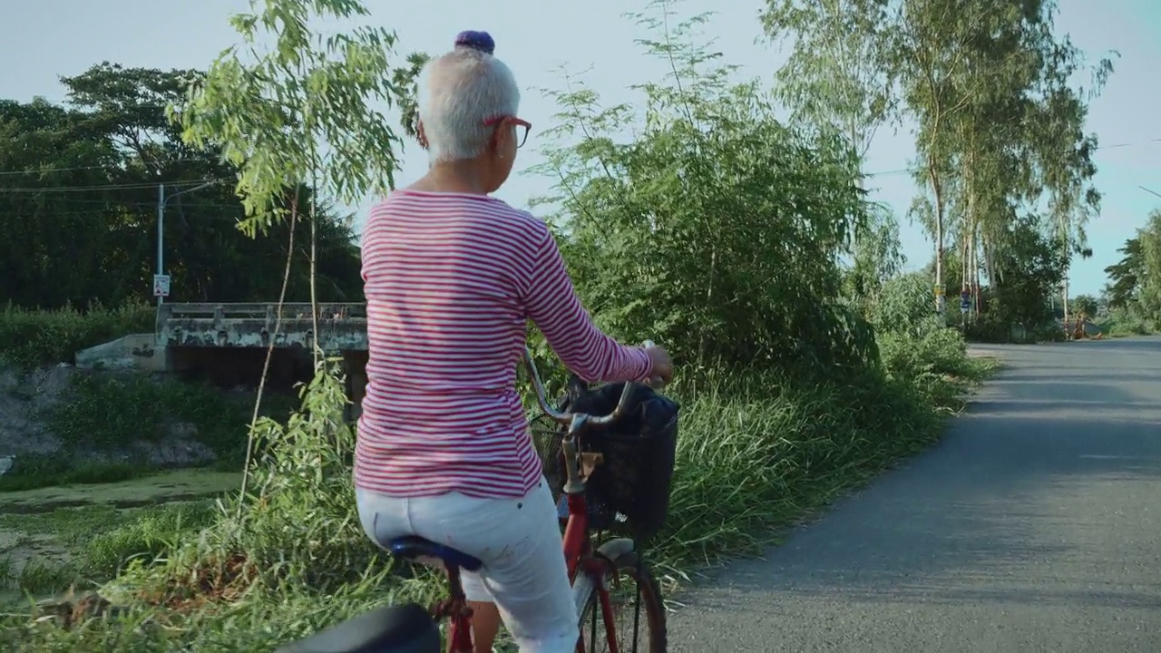 老年妇女骑着自行车穿过夕阳，在退休后的非城市，度假，当地自驾游。