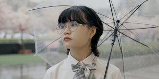 可爱的亚洲女生，穿着校服，打着伞，站在街上