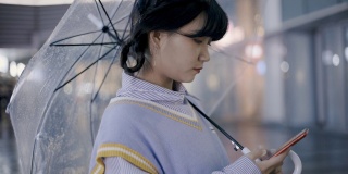 美丽的日本女性站在雨后的街道上使用智能手机