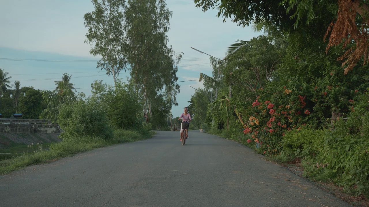 老年妇女骑着自行车穿过夕阳，在退休后的非城市，度假，当地自驾游。