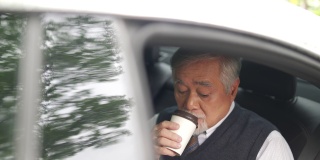 4K亚洲资深商人坐在汽车后座，一边喝着热咖啡，一边在数码平板电脑上工作