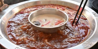 人们用筷子将肉放入辛辣的中国火锅的特写。