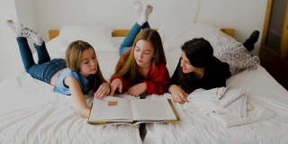 三个快乐的姐妹躺在卧室里看书。