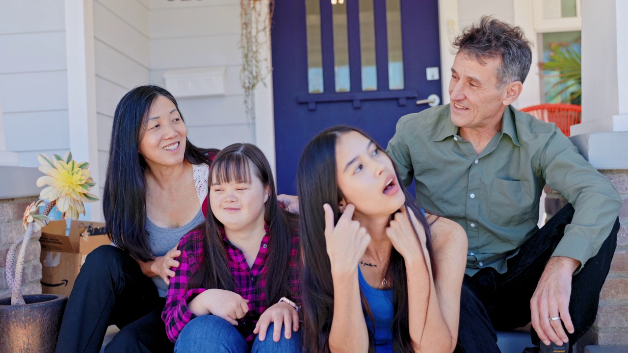 不同的家庭坐在他们的家门口。一个女儿患有唐氏综合症。