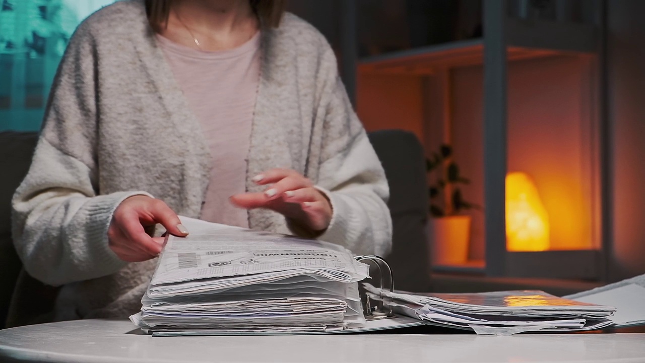女人翻看家庭文件或公用事业帐单的文件夹，坐在家里的桌子前，晚上，慢动作