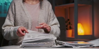 女人翻看家庭文件或公用事业帐单的文件夹，坐在家里的桌子前，晚上，慢动作
