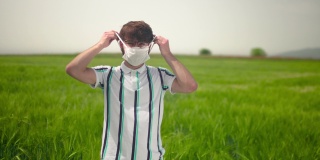 年轻男子穿着便服，在绿色的田野里散步，戴上防护口罩，遮住嘴和鼻子。