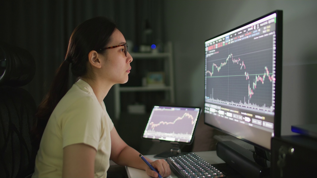 女性在家庭办公室看着电脑屏幕上的股票市场数据，同时与电脑工作