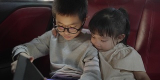 亚洲的兄弟姐妹在车里用数码平板电脑看视频或电影时放松，亚洲的家庭生活方式带有科技设备的概念