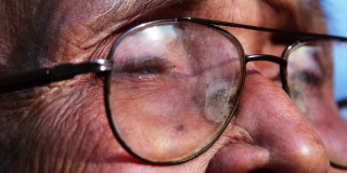 一位戴着眼镜的老人的特写脸，在阳光下眺望远方。眼光和老年人的观念