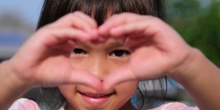 一个亚洲小女孩的特写镜头，看着相机，用她的手做一个心形。心形象征着爱。