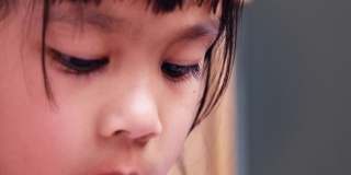 亚洲小孩在室内看书的特写。美丽的棕色眼睛，长长的睫毛。