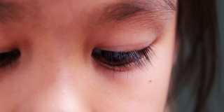 亚洲小孩在室内看书的特写。美丽的棕色眼睛，长长的睫毛。
