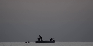两个渔民在海上的小船上拉着网的剪影