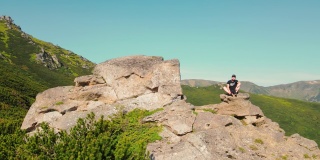 年轻的雄性坐在山顶从空中看到。一个徒步旅行者坐在悬崖边上，眺望远方。展望未来。爬山的人在山顶休息