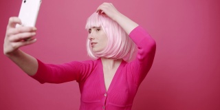 年轻漂亮的女人与粉红色的头发拍照，自我孤立的粉红色背景