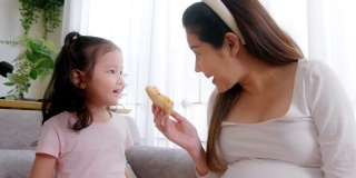 孕妇和可爱的小女儿在家里吃着不健康的披萨。