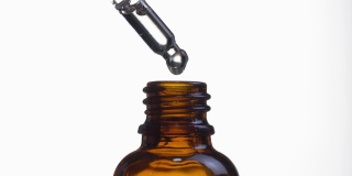 特写的化妆品油从移液器滴到瓶子上的白色背景。
