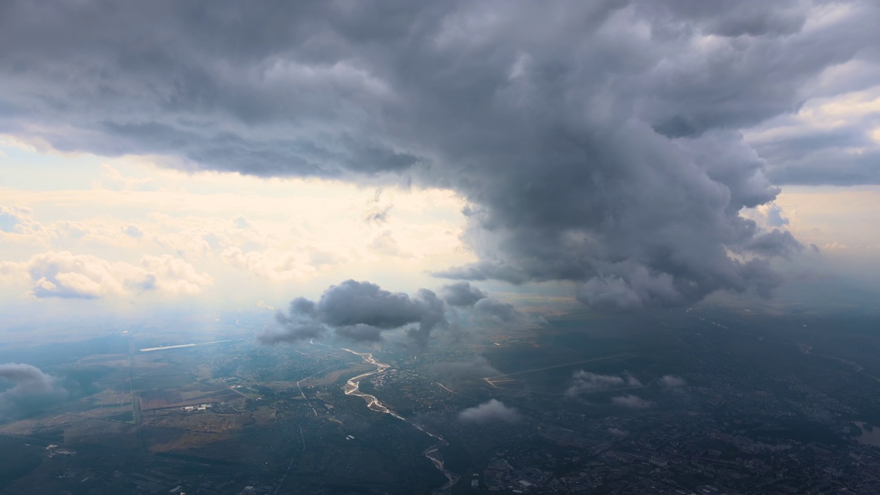 从高空的飞机窗口鸟瞰，远处的城市被暴雨前形成的蓬松的积云所覆盖